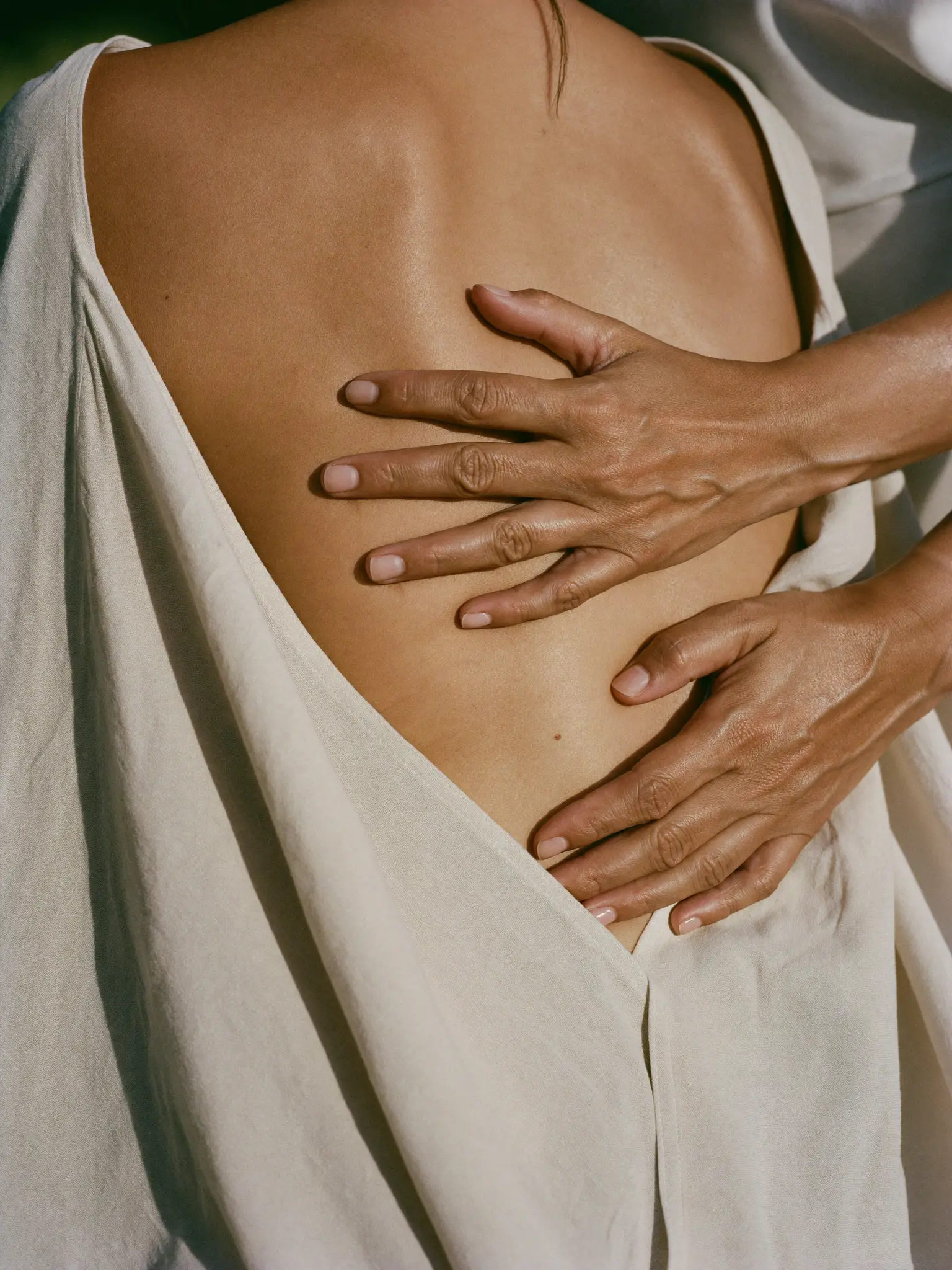 A practitioner's hands working along a client's back, draped in bone linen