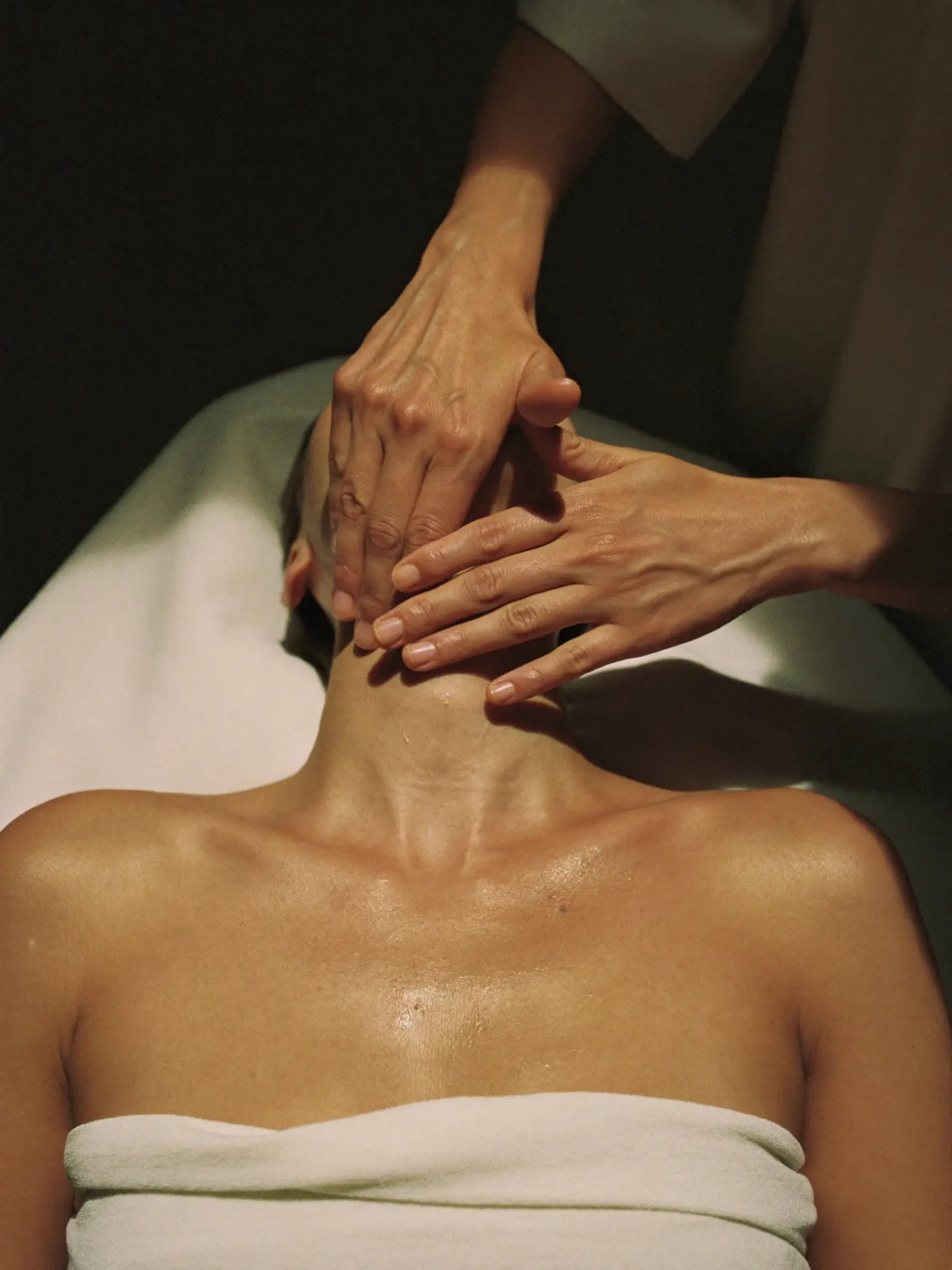 A therapist's hands mid-stroke at the transition from décolleté to neck
