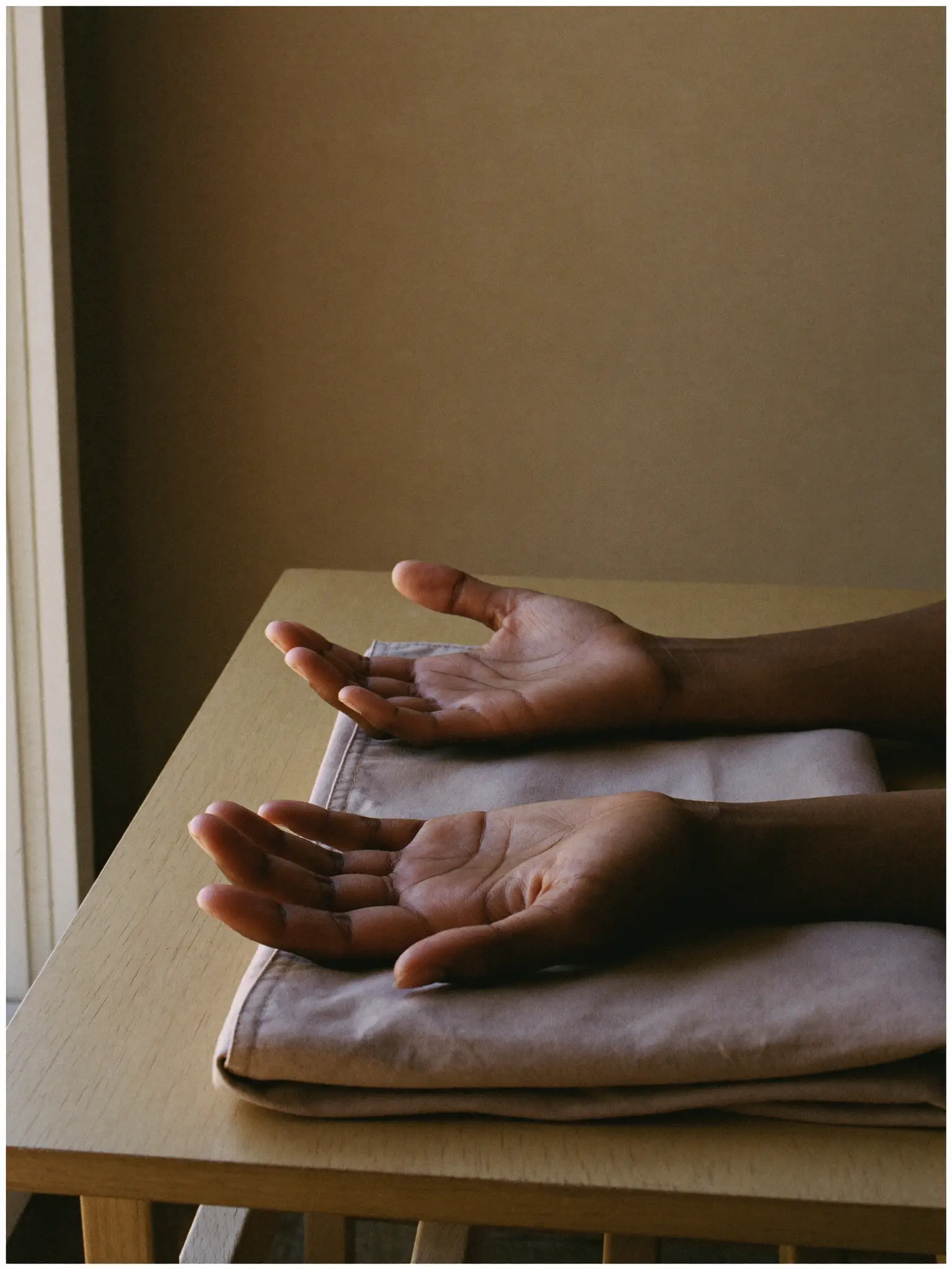 A practitioner's hands at rest, palms open on folded linen by a window