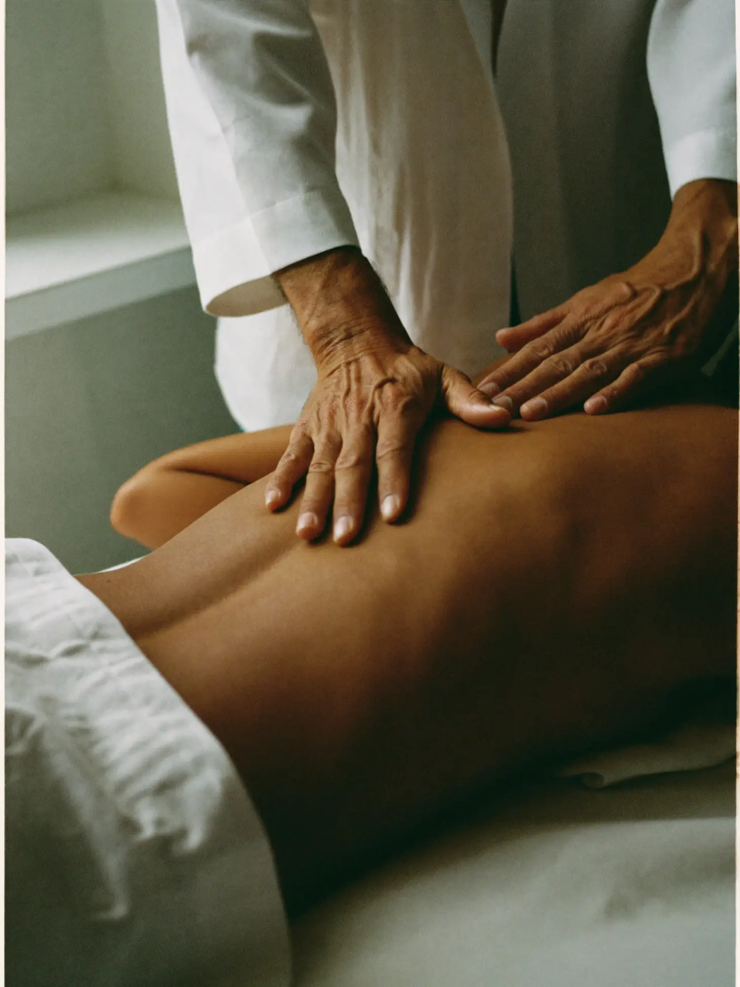 A practitioner's hands mid-stroke along a client's upper back