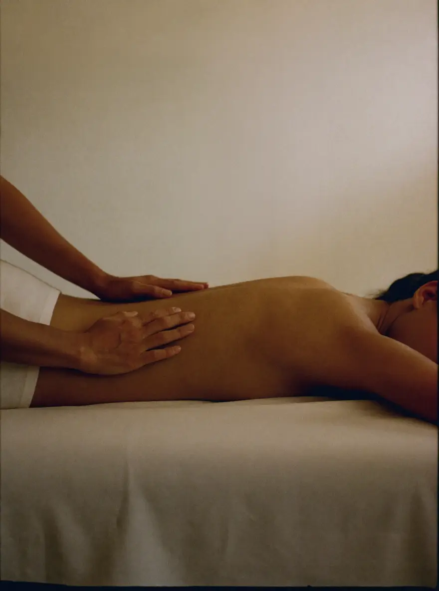 A therapist's hands resting still on a client's back, reading the body before treatment