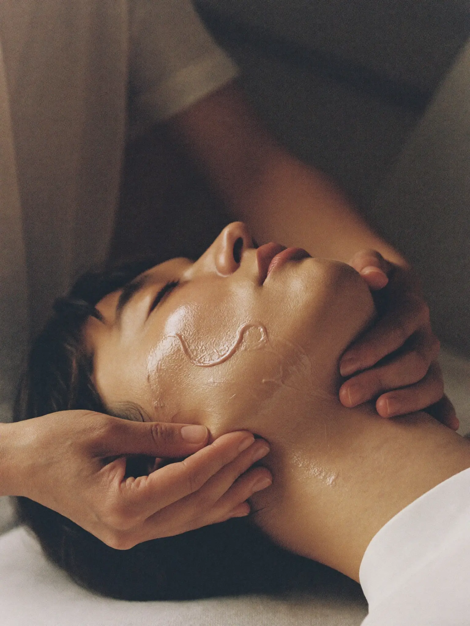 Hands supporting a reclining person’s jaw and neck in warm light.